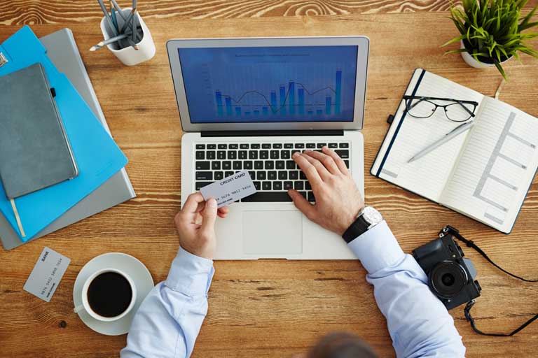 Man sitting down having a coffee checking credit card reports on his laptop