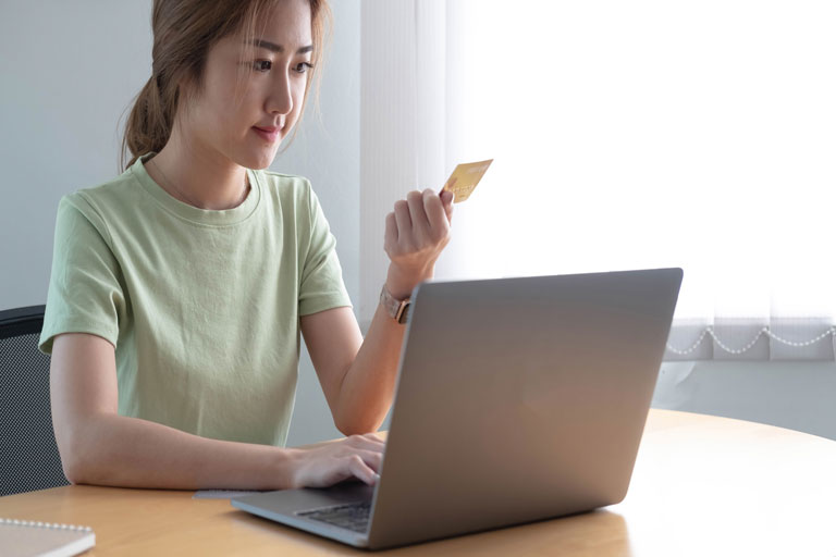 Woman checking the numbers in the back of her credit card about to make an online purchase on her laptop