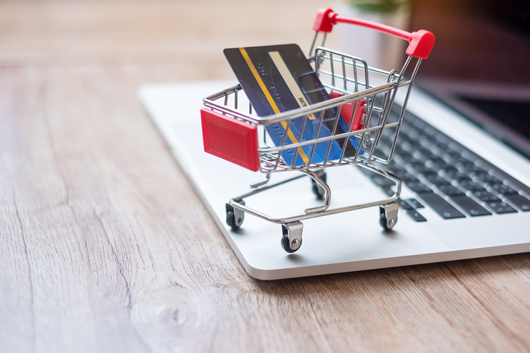 Small shopping cart with a credit card inside, on top of a laptop