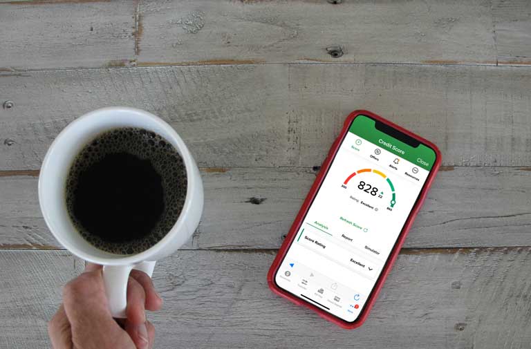 man holding a coffee mug while checking his credit score on a smartphone
