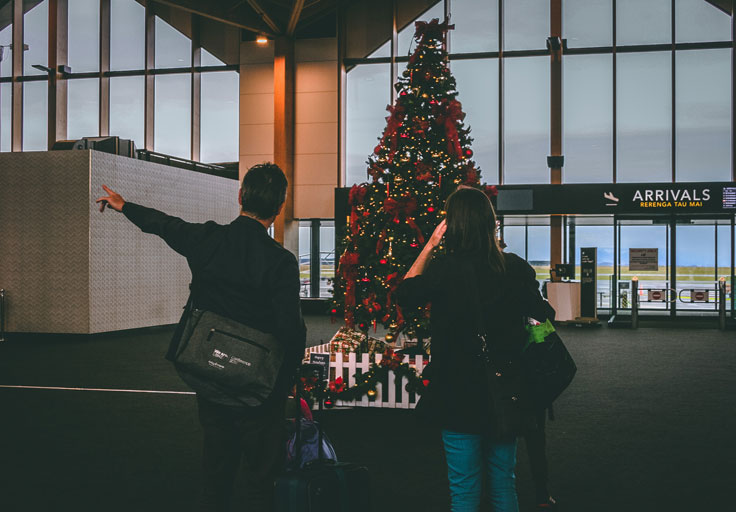 Couple at an airport in front of a christmas tree