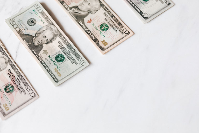 US dollar bills laying on a white marble table