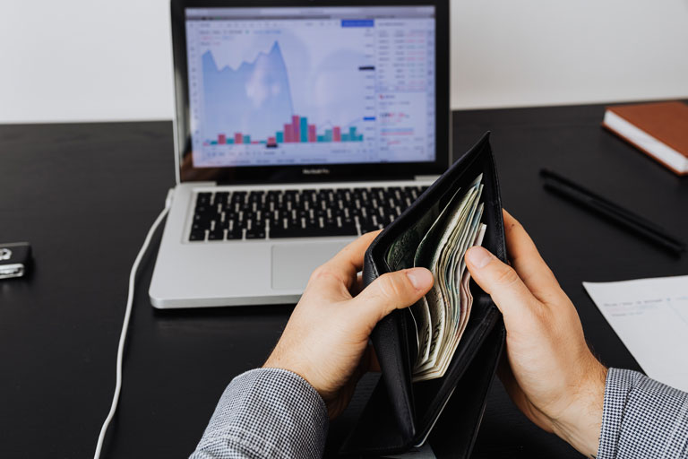 Man checking a wallet full of cash in front of a laptop