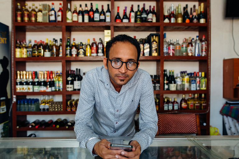 Liquor store owner laying on a counter with a phone in his hand