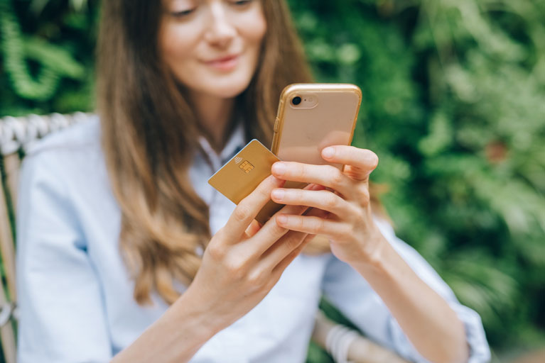 Woman paying for an online purchase on her phone while holding a creditcard