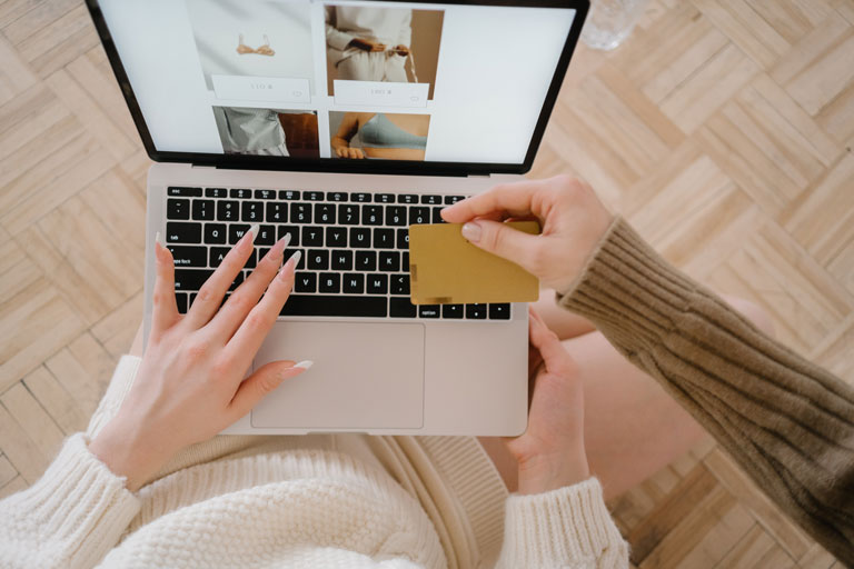 Woman handing a credit card to another woman shopping online on her laptop