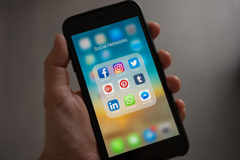 Man holding up an iphone showing social media app icons on the screen