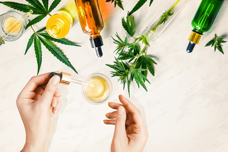 Woman adding a drop of cbd to her drink with cannabis plants around the table