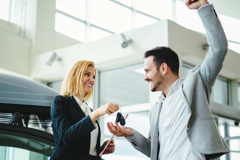 Happy male customer at a car dealership lifting up his arms after purchasing a car