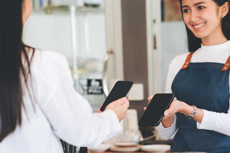 Female barista holding up a phone for a customer to pay with her phone at a cafe
