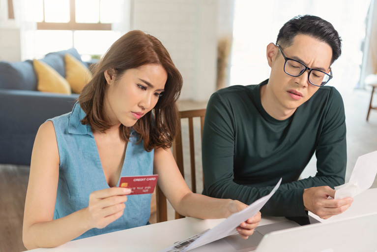 Worried asian couple sitting inside their house looking at a credit card statement