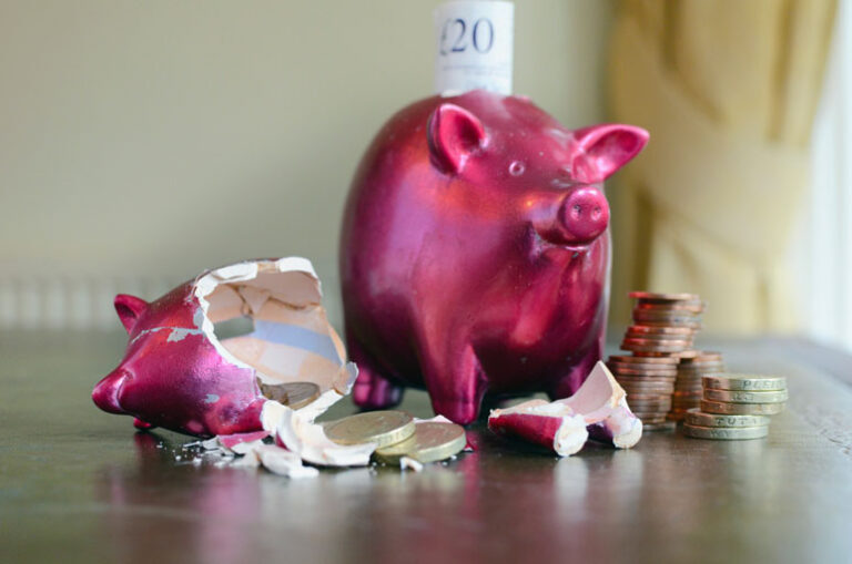 2 red piggy banks on a table but one of them is broken