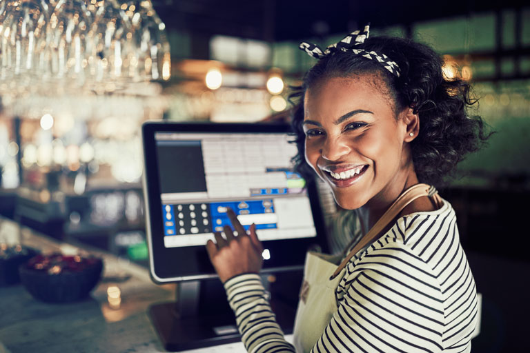 Happy african american waitress touching the screen of a point of sale system inside a restaurant