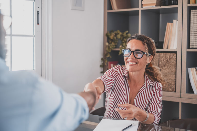 Woman with glasses shaking a man's hand inside an office