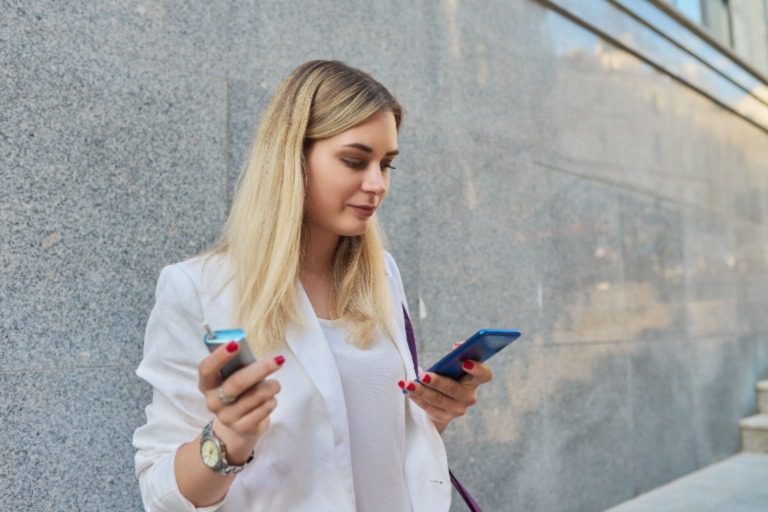 Young female checking her phone and vaping outside of her office