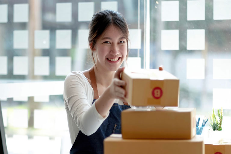 Young asian woman smiling while stacking packages on top of each other for her small business
