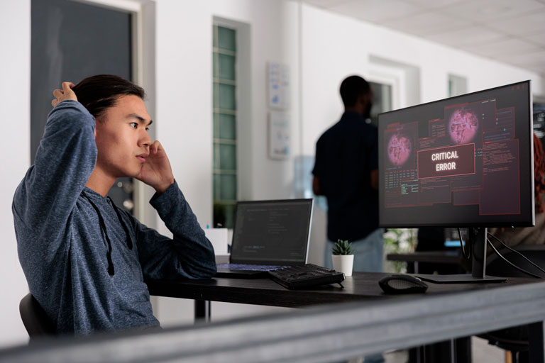 Stressed young professional scratching his head while talking on the phone looking at an critical error message on the screen of his computer