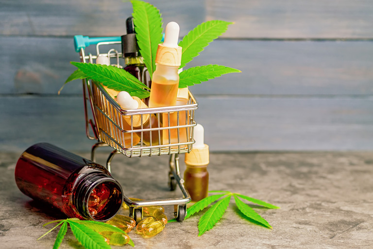 Small shopping cart filled with containers cbd oils, marijuana plants and CBD pills