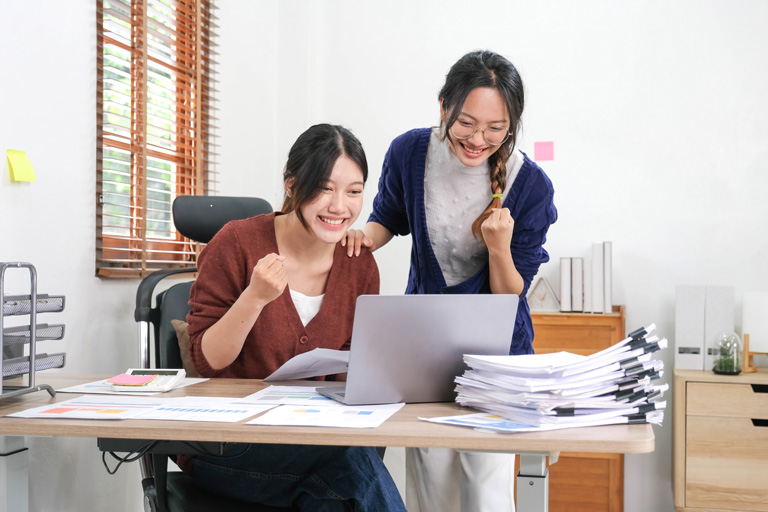 Two young asian woman celebrating in front of a laptop inside their home