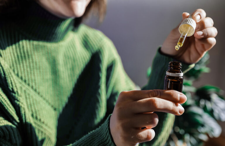 Woman putting a drop of CBD oil with an eye dropper inside a small container