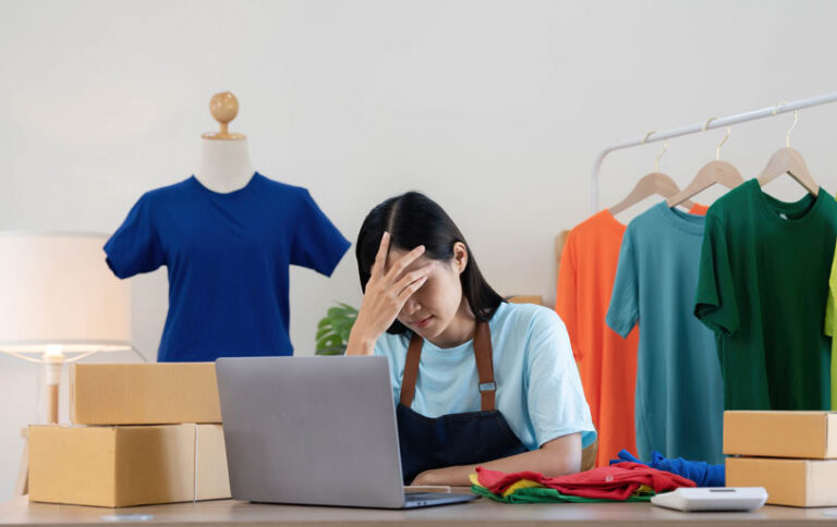 Frustrated online clothes business owner in front of a laptop with her hand in her forehead