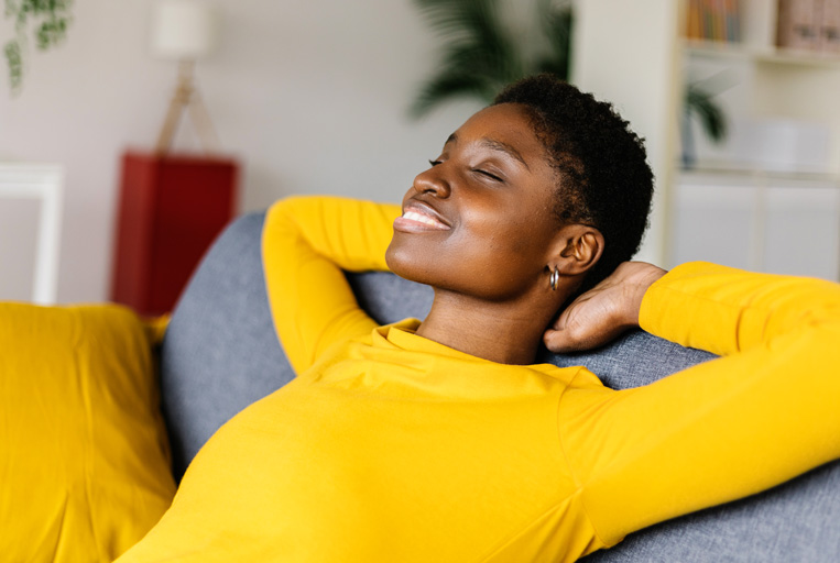 African american woman relaxing on a sofa with her eyes closed and arms behind her neck