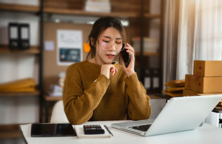 Young Asian american woman talking on the phone while running a home business