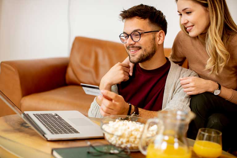 Young couple making an online purchase while eating popcorn and drinking orange juice