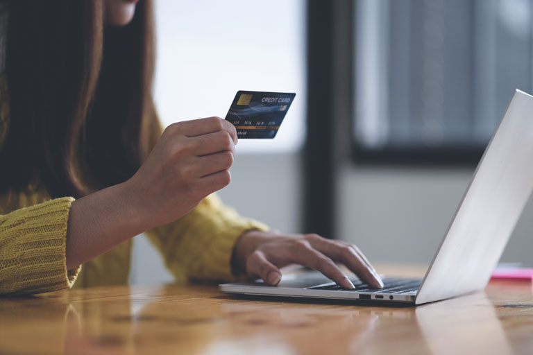 Woman checking the numbers on the back of a credit card in front of a laptop